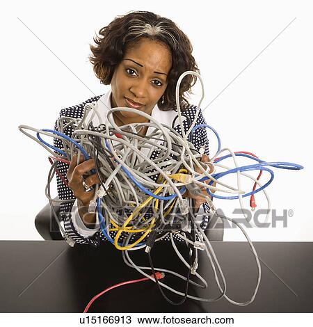 Stock Image - Businesswoman holding bundle of tangled computer cords with overwhelmed look on her face.. Fotosearch