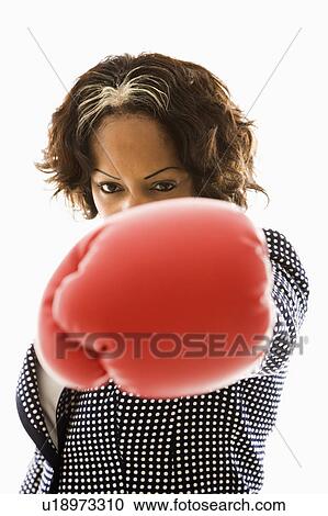 Stock Image - Businesswoman wearing boxing gloves punching. Fotosearch