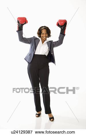 Stock Photo - Businesswoman wearing boxing gloves holding arms up in victory stance and smiling.. Fotosearch