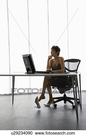 Stock Image - Caucasian businesswoman sitting at desk with computer in office.. Fotosearch