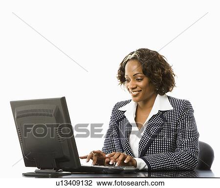 Stock Image - Smiling businesswoman sitting at desk typing on computer. Fotosearch