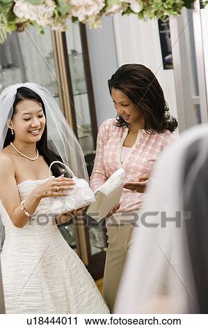 Stock Image - African-American woman helping Asian bride pick out handbag.. Fotosearch