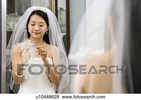 Stock Photo - Asian bride looking at bouquet in mirror.. Fotosearch