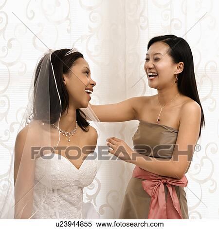 Stock Photography - Asian bridesmaid laughing with African-American bride.. Fotosearch
