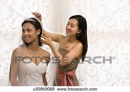 Stock Photo - Bridesmaid adjusting veil of a bride.. Fotosearch