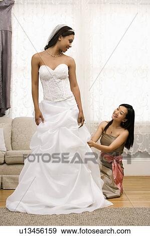 Stock Photo - Bridesmaid fixing bride's dress. Fotosearch