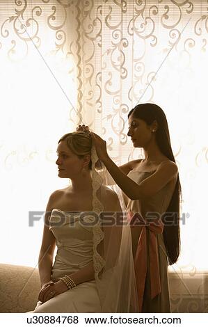 Stock Photo - Bridesmaid placing veil on a bride. Fotosearch
