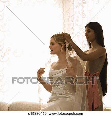 Stock Photograph - Bridesmaid placing veil on bride. Fotosearch