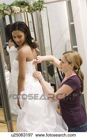 Stock Photo - Caucasian seamstress helping African-American bride in bridal shop.. Fotosearch