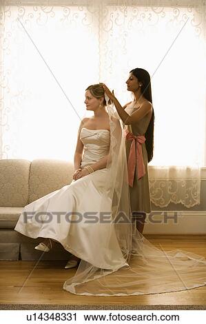 Stock Image - Indian bridesmaid placing veil on Caucasian bride.. Fotosearch