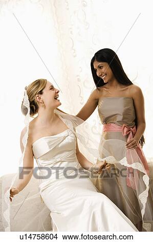 Picture - Indian maid of honor holding Caucasian bride's veil.. Fotosearch