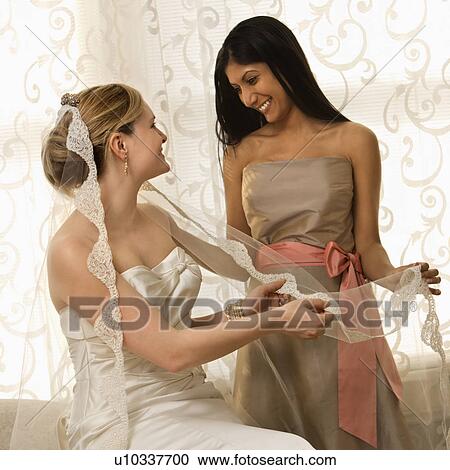 Stock Image - Indian maid of honor holding Caucasian bride's veil.. Fotosearch
