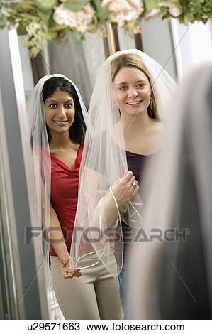 Stock Image - Women trying on veils and looking in mirror. Fotosearch