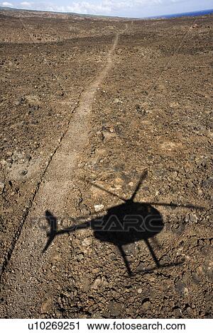 Stock Image - Pathway leading through rocky terrain with shadow of helicopter flying overhead in Maui, Hawaii.. Fotosearch