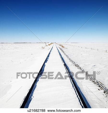 Snow covered railroad tracks leading to a blue sky View Large Photo Image Stock Photo - Snow covered railroad tracks leading to a blue sky . Fotosearch