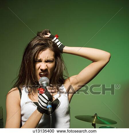 Stock Image - Caucasian female singing into microphone and pulling her hair.. Fotosearch