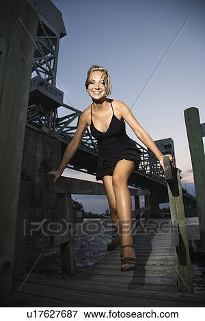 Caucasian mid-adult blonde woman wearing little black dress walking on dock along bridge. View Large Photo Image Stock Photo - Caucasian mid-adult blonde woman wearing little black dress walking on dock along bridge.. Fotosearch