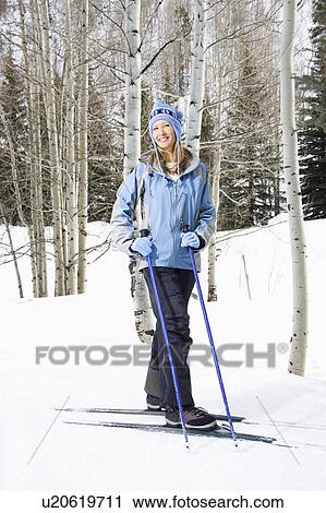 Stock Image - Female skier wearing blue ski clothing standing on ski slope smiling. Fotosearch
