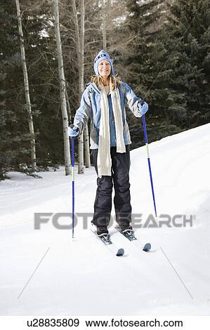 Stock Photo - Mid adult female skier wearing blue ski clothing standing on ski slope smiling. Fotosearch