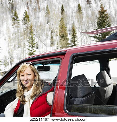 Stock Photo - Pretty woman sitting in vehicle wearing winter clothes in rural snowy Colorado smiling. Fotosearch