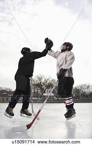 Two boys in ice hockey uniforms giving each other high five on ice rink View Large Photo Image Picture - Two boys in ice hockey uniforms giving each other high five on ice rink. Fotosearch