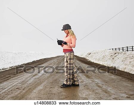 Woman in winter clothes standing on muddy dirt road looking at cell phone View Large Photo Image Stock Image - Woman in winter clothes standing on muddy dirt road looking at cell phone. Fotosearch