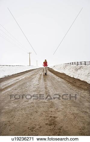 Young woman in winter clothes walking alone down muddy dirt road with snow on edges of road View Large Photo Image Stock Image - Young woman in winter clothes walking alone down muddy dirt road with snow on edges of road. Fotosearch