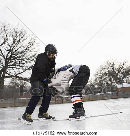 Stock Image - Ice hockey player boy roughing up another player on the ice rink.. Fotosearch