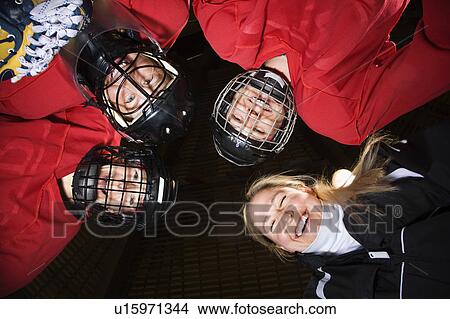 Low angle of female hockey players in huddle with coach smiling. View Large Photo Image Picture - Low angle of female hockey players in huddle with coach smiling.. Fotosearch