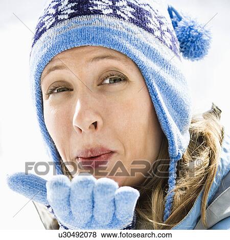 Stock Photo - Portrait of attractive smiling mid adult Caucasian blond woman wearing blue ski cap and gloves blowing kiss at viewer.. Fotosearch