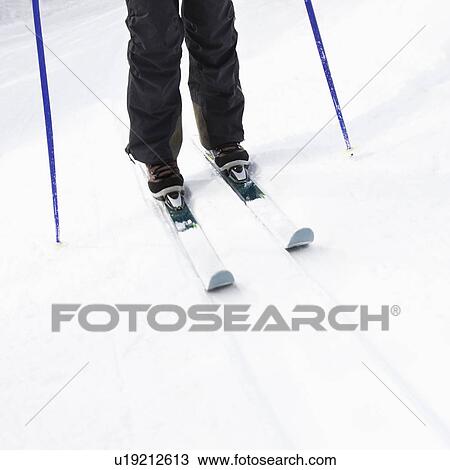 Stock Image - Skier legs, boots, poles and skis standing on slope. Fotosearch