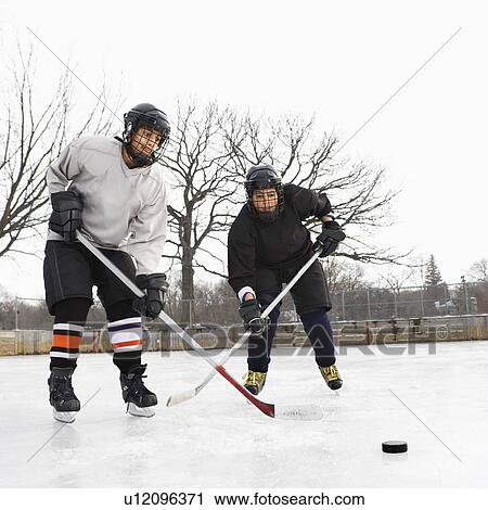 Two boys in ice hockey uniforms playing hockey on ice rink. View Large Photo Image Stock Image - Two boys in ice hockey uniforms playing hockey on ice rink.. Fotosearch