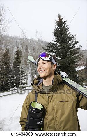 Winter clothing walking in snow carrying ski equipment and smiling View Large Photo Image Stock Photo - Winter clothing walking in snow carrying ski equipment and smiling. Fotosearch