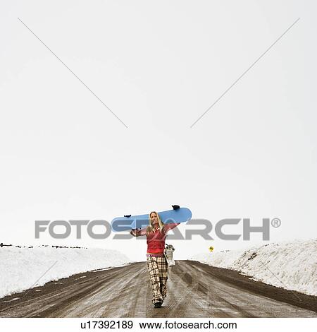 Young woman in winter clothes walking alone down muddy dirt road carrying snowboard and boots View Large Photo Image Stock Photo - Young woman in winter clothes walking alone down muddy dirt road carrying snowboard and boots. Fotosearch