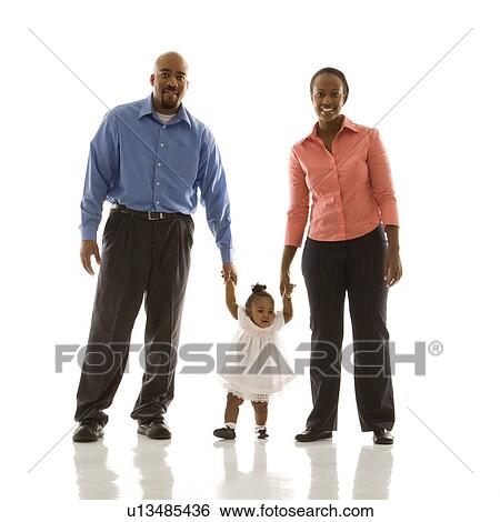 Stock Photograph - African American man and woman standing holding up infant girl by her hands against white background.. Fotosearch