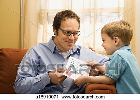 Stock Image - Caucasian boy giving mid adult father a drawing.. Fotosearch