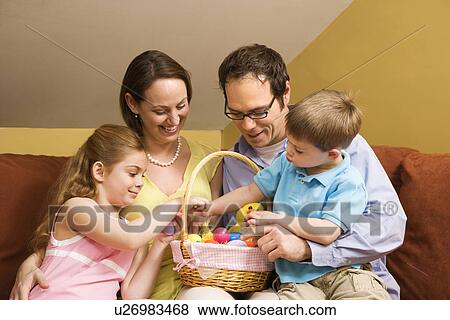 Stock Photo - Caucasian family on couch looking at Easter basket. . Fotosearch