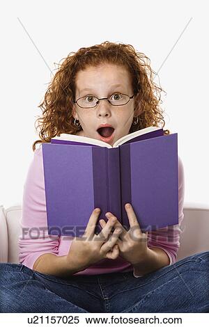 Stock Photography - Caucasian female child sitting reading book looking surprised.. Fotosearch