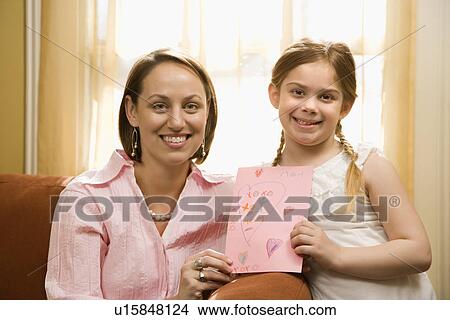 Picture - Caucasian girl giving mid adult mother a drawing and looking at viewer.. Fotosearch