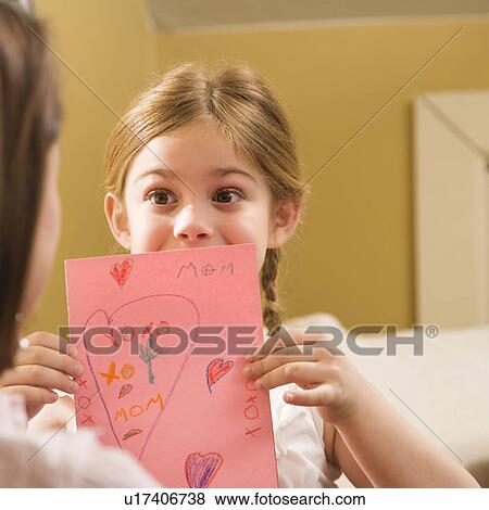 Stock Photo - Caucasian girl giving mid adult mother a drawing.. Fotosearch