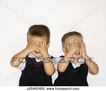Stock Photography - Caucasian male children twins with hands over eyes.. Fotosearch