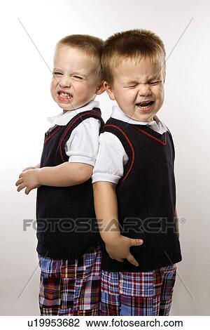 Stock Image - Caucasian twin boys crying standing against white background.. Fotosearch