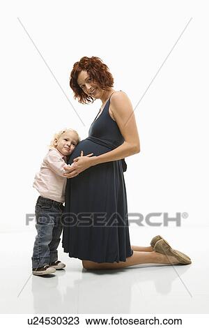 Caucasion mid-adult attractive pregnant woman kneeling in front of female toddler who is pressing ear against belly. View Large Photo Image Stock Image - Caucasion mid-adult attractive pregnant woman kneeling in front of female toddler who is pressing ear against belly.. Fotosearch
