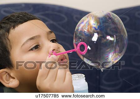 Stock Photography - Hispanic boy blowing large soap bubble.. Fotosearch