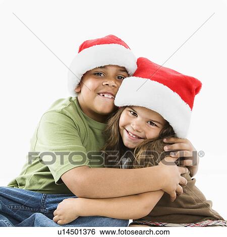 Stock Photograph - Hispanic brother and sister wearing santa hats hugging. Fotosearch