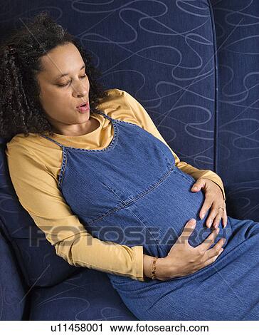 Stock Image - Portrait of young pregnant female with hands on stomach.. Fotosearch