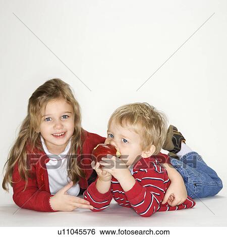 Studio portrait of Caucasian girl with arm around boy eating apple against white background. View Large Photo Image Stock Photograph - Studio portrait of Caucasian girl with arm around boy eating apple against white background.. Fotosearch