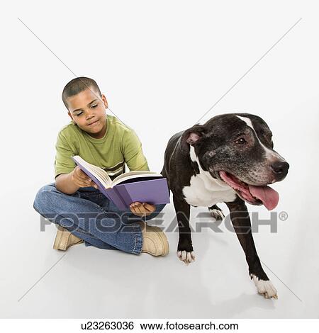Stock Photograph - Young hispanic boy reading book while his dog sits nearby.. Fotosearch