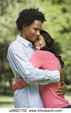 Attractive couple smiling and embracing in park. View Large Photo Image Stock Image - Attractive couple smiling and embracing in park.. Fotosearch