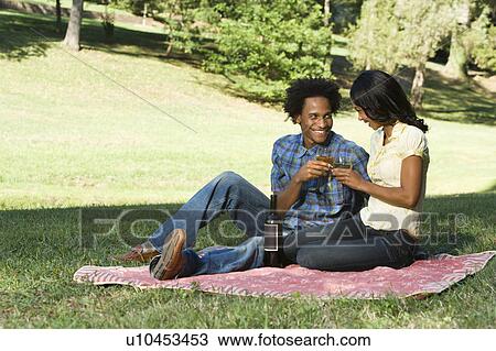 Stock Image - Couple having romantic picnic in park toasting wine. Fotosearch